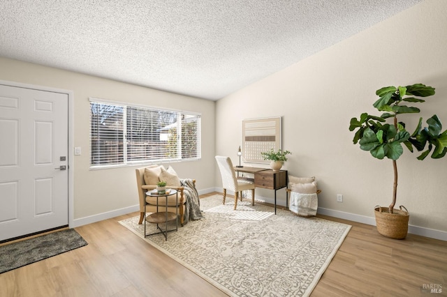 foyer featuring lofted ceiling, baseboards, light wood-style flooring, and a textured ceiling