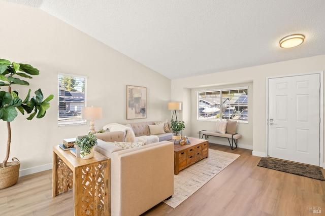 living room featuring a healthy amount of sunlight, light wood-type flooring, vaulted ceiling, and a textured ceiling