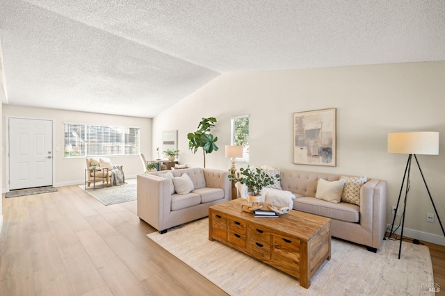 living area featuring a healthy amount of sunlight, vaulted ceiling, light wood-style flooring, and a textured ceiling