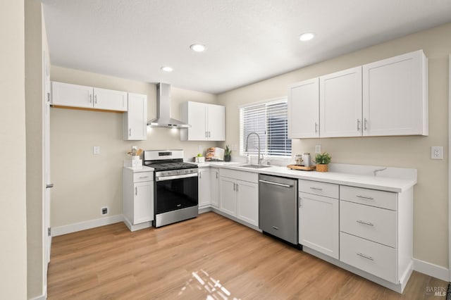 kitchen featuring a sink, white cabinets, light countertops, wall chimney range hood, and appliances with stainless steel finishes