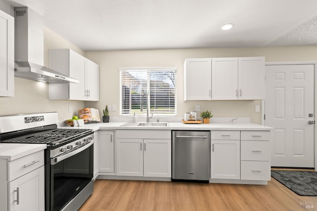 kitchen with stainless steel appliances, white cabinets, light countertops, and wall chimney range hood