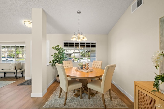 dining space with visible vents, vaulted ceiling, a textured ceiling, a chandelier, and light wood-type flooring