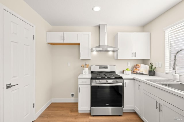 kitchen with white cabinets, stainless steel gas range, wall chimney exhaust hood, and light countertops