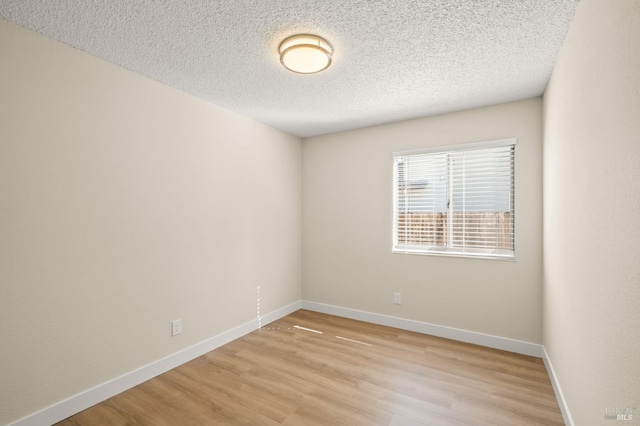 empty room featuring a textured ceiling, light wood-style flooring, and baseboards