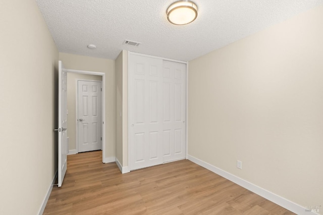 unfurnished bedroom featuring baseboards, a closet, visible vents, and light wood-style floors