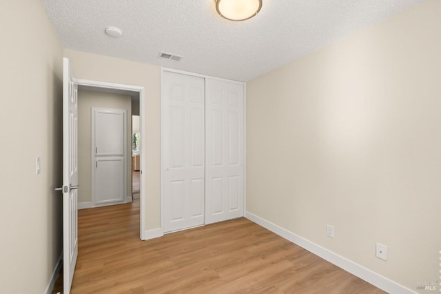 unfurnished bedroom with baseboards, visible vents, a textured ceiling, light wood-type flooring, and a closet