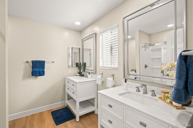 full bathroom with wood finished floors, two vanities, baseboards, a sink, and a shower stall