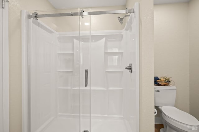 bathroom featuring a textured wall, a stall shower, and toilet