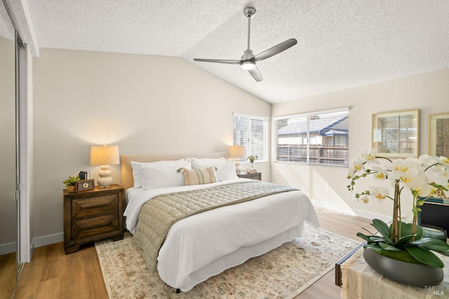 bedroom with light wood finished floors, lofted ceiling, a ceiling fan, a textured ceiling, and baseboards