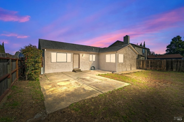 back of house at dusk featuring stucco siding, a fenced backyard, and a patio