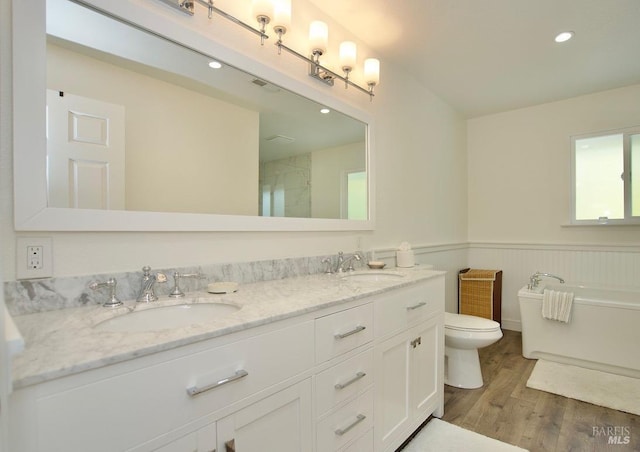 bathroom with toilet, a wainscoted wall, a sink, and wood finished floors