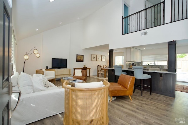 living room featuring recessed lighting, light wood-type flooring, visible vents, and ornate columns