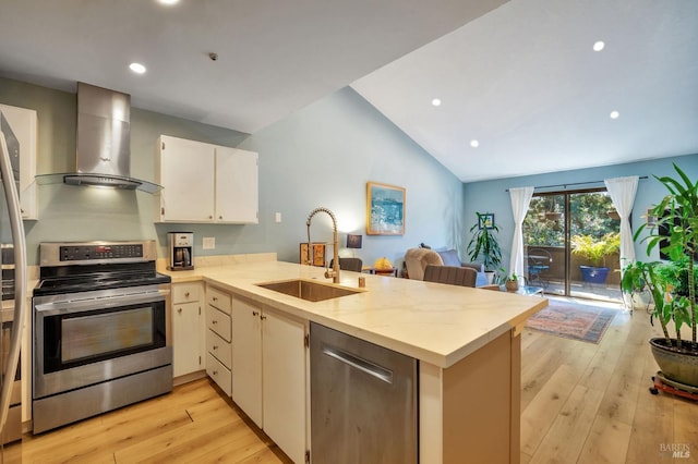 kitchen featuring stainless steel appliances, open floor plan, a sink, wall chimney range hood, and a peninsula