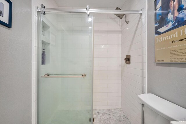 bathroom featuring a textured wall, a stall shower, and toilet