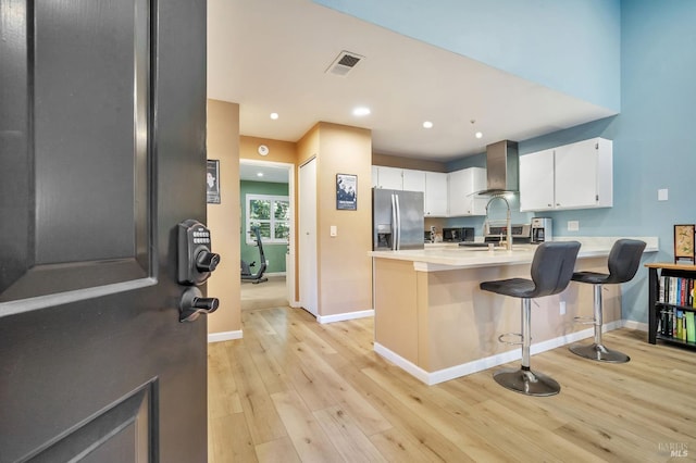 kitchen with stainless steel appliances, light countertops, visible vents, wall chimney range hood, and a peninsula