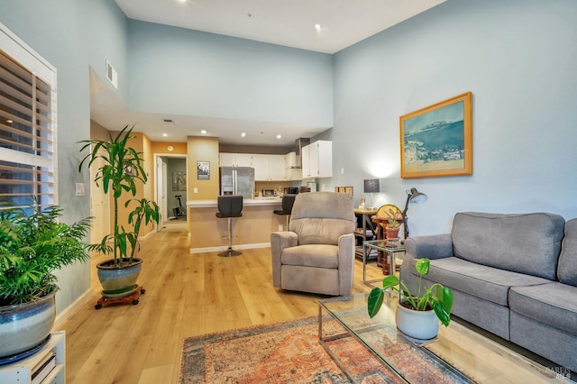 living area with light wood-style floors, baseboards, visible vents, and a high ceiling