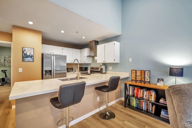 kitchen with stainless steel appliances, light wood-style flooring, a sink, a peninsula, and wall chimney exhaust hood