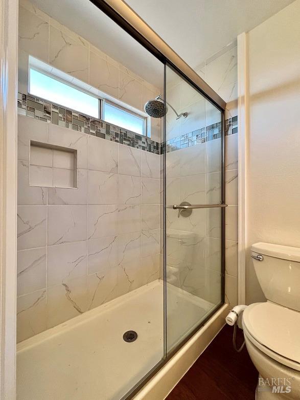 bathroom featuring a tile shower, wood finished floors, and toilet