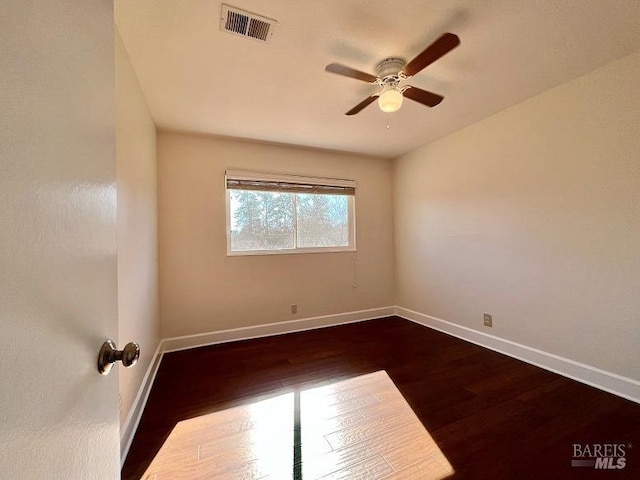 spare room with a ceiling fan, dark wood-style flooring, visible vents, and baseboards