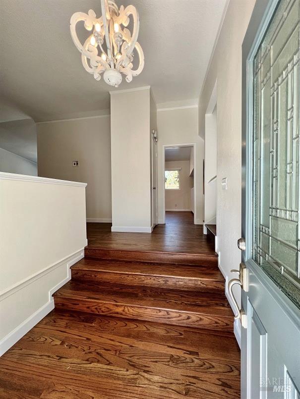 foyer entrance featuring stairway, baseboards, a chandelier, and dark wood-type flooring