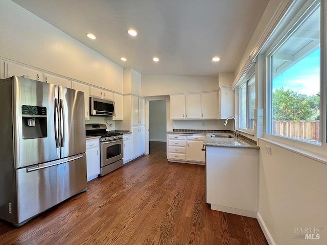 kitchen with dark wood-style flooring, stainless steel appliances, stone counters, white cabinetry, and a sink