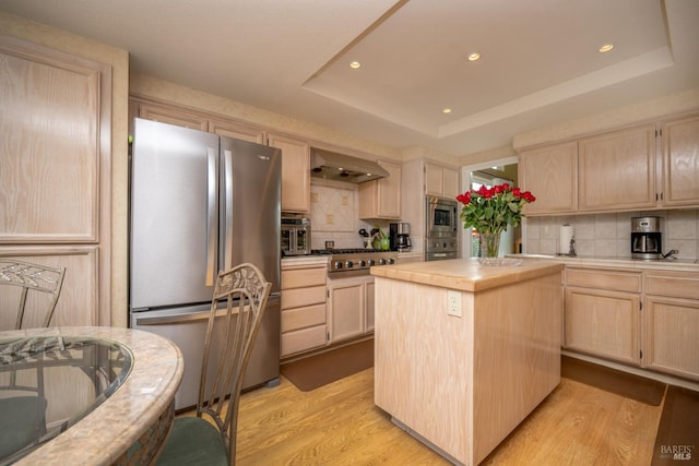 kitchen featuring light brown cabinets, stainless steel appliances, a kitchen island, light countertops, and a tray ceiling