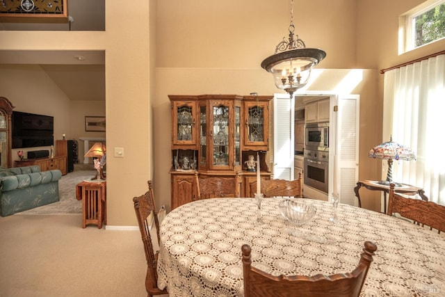 carpeted dining space with a towering ceiling, a fireplace, and a notable chandelier