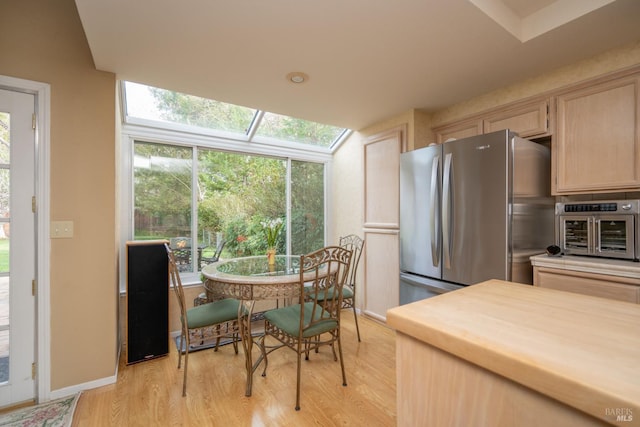 kitchen with light wood-style floors, freestanding refrigerator, light brown cabinets, and a skylight