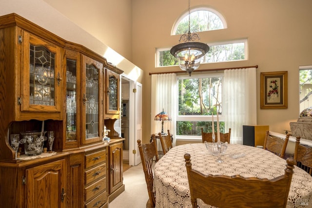 dining space with light carpet, a towering ceiling, and an inviting chandelier