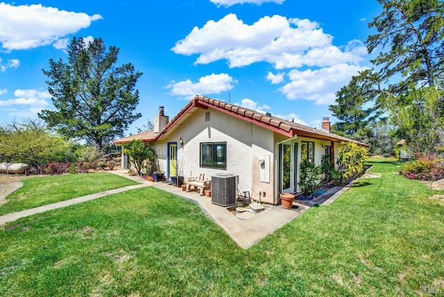 rear view of property with a patio, a chimney, a lawn, and stucco siding