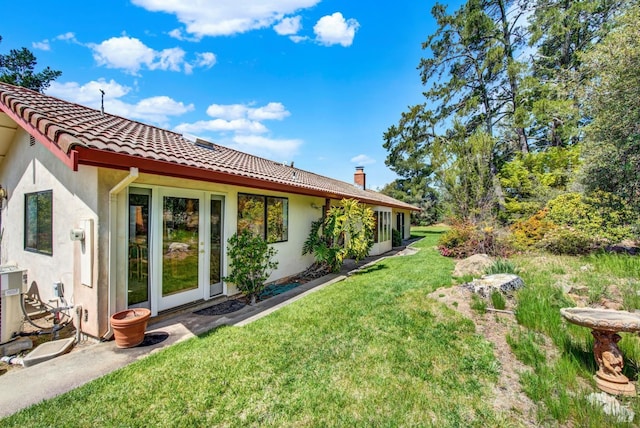 rear view of property featuring a tiled roof, a lawn, a chimney, and stucco siding