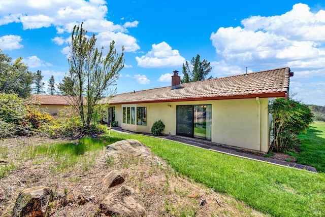 rear view of property with a tile roof, a yard, a chimney, and stucco siding