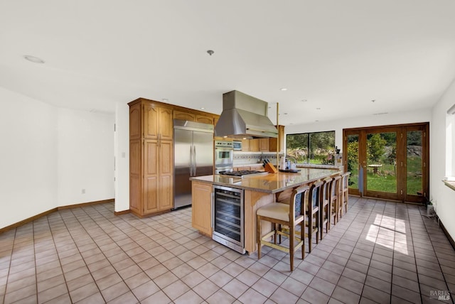 kitchen featuring wine cooler, a breakfast bar, appliances with stainless steel finishes, island exhaust hood, and a center island with sink