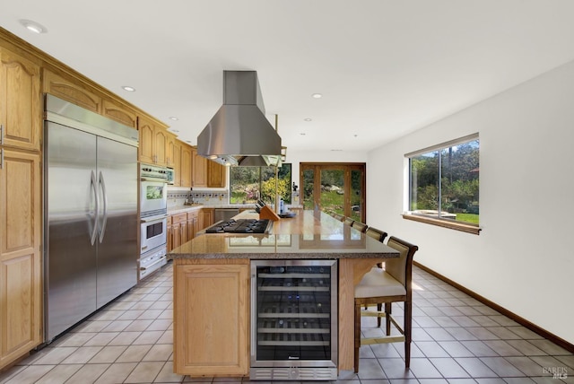 kitchen featuring a center island, island exhaust hood, light tile patterned floors, stainless steel appliances, and beverage cooler