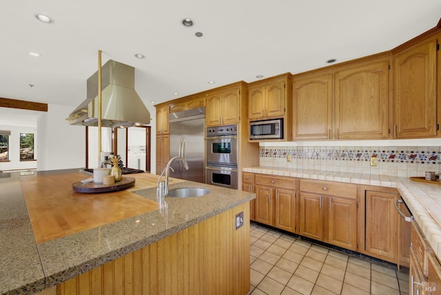 kitchen featuring built in appliances, a sink, light countertops, decorative backsplash, and island exhaust hood