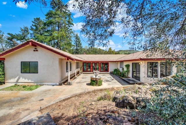 back of house with french doors, a tile roof, a chimney, stucco siding, and a patio area