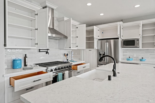 kitchen featuring white cabinets, appliances with stainless steel finishes, wall chimney range hood, light stone countertops, and open shelves