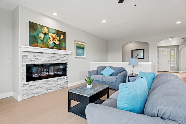 living room with arched walkways, a fireplace, recessed lighting, wood finished floors, and baseboards