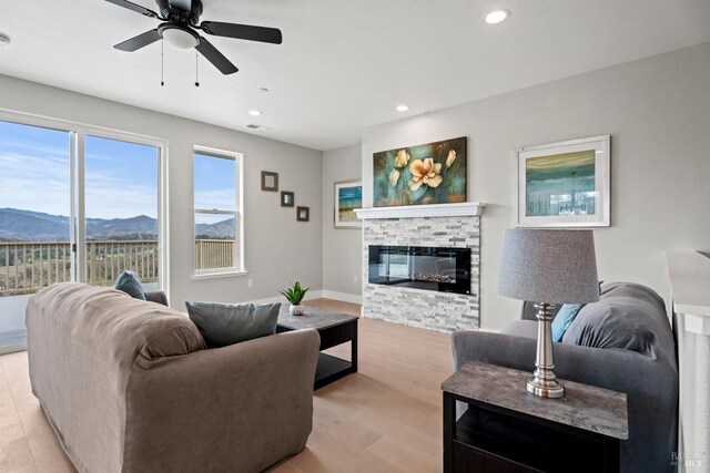 living area featuring light wood finished floors, recessed lighting, a mountain view, a stone fireplace, and baseboards