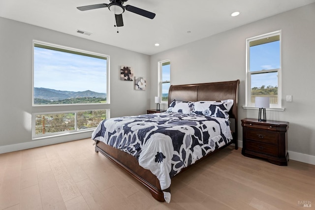 bedroom with light wood-style floors, visible vents, multiple windows, and a mountain view