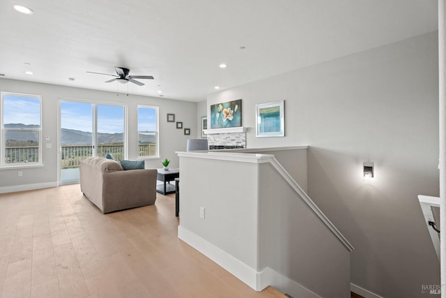 living area with a fireplace, light wood finished floors, recessed lighting, a mountain view, and baseboards