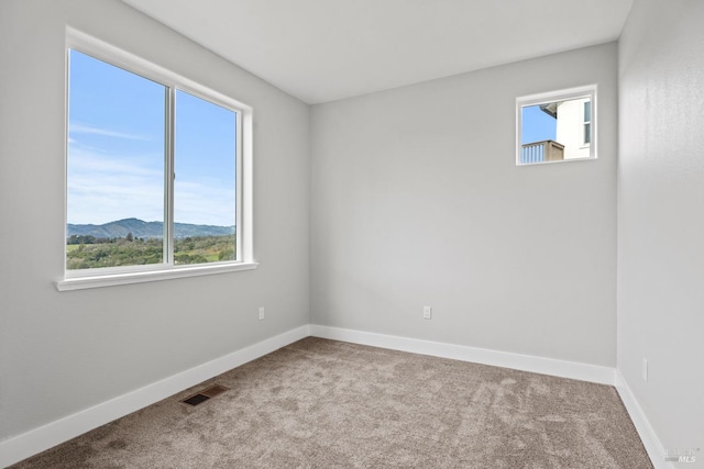 unfurnished room featuring light carpet, baseboards, visible vents, and a mountain view