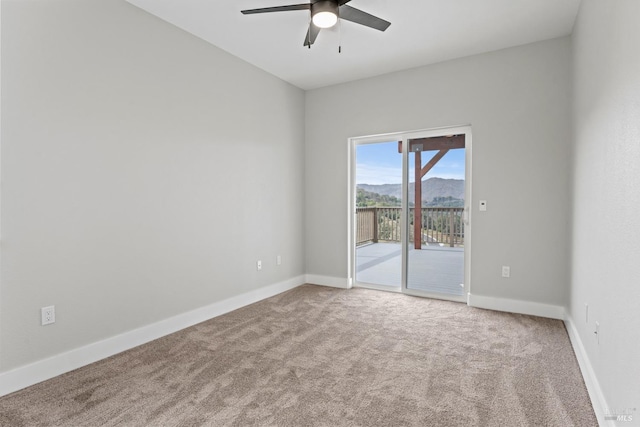 carpeted empty room with ceiling fan, a mountain view, and baseboards