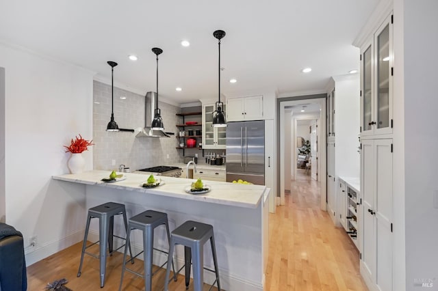 kitchen with built in fridge, tasteful backsplash, light wood-style flooring, wall chimney range hood, and a peninsula