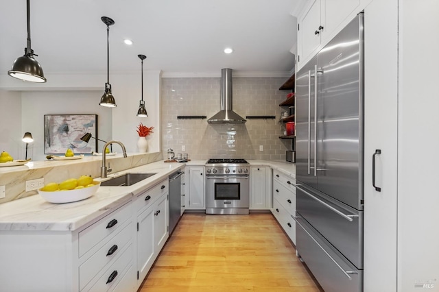 kitchen with open shelves, high end appliances, light wood-style floors, a sink, and wall chimney exhaust hood