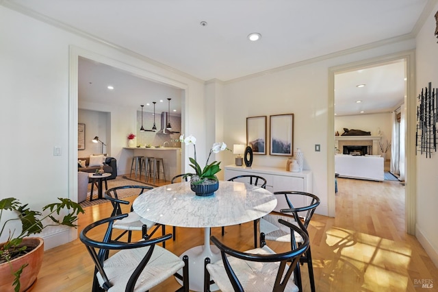 dining space featuring recessed lighting, a fireplace, crown molding, and light wood finished floors