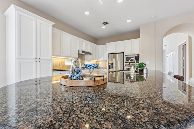 kitchen with under cabinet range hood, appliances with stainless steel finishes, white cabinets, and dark stone counters