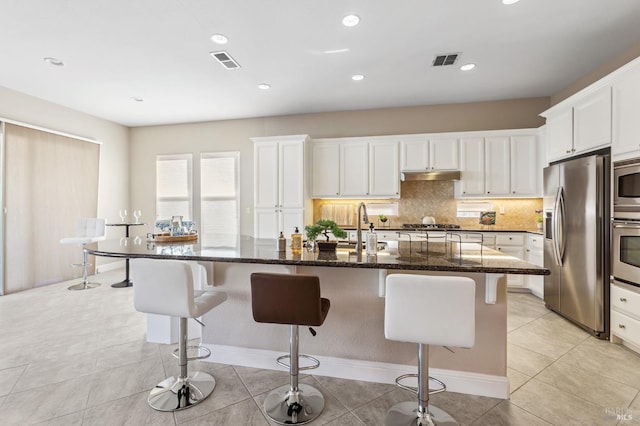 kitchen with a kitchen island with sink, appliances with stainless steel finishes, visible vents, and white cabinets