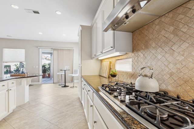 kitchen featuring stainless steel gas cooktop, visible vents, white cabinets, wall chimney range hood, and dark stone countertops