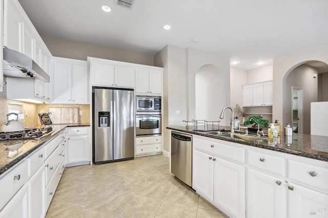 kitchen with appliances with stainless steel finishes, dark stone countertops, a sink, and ventilation hood